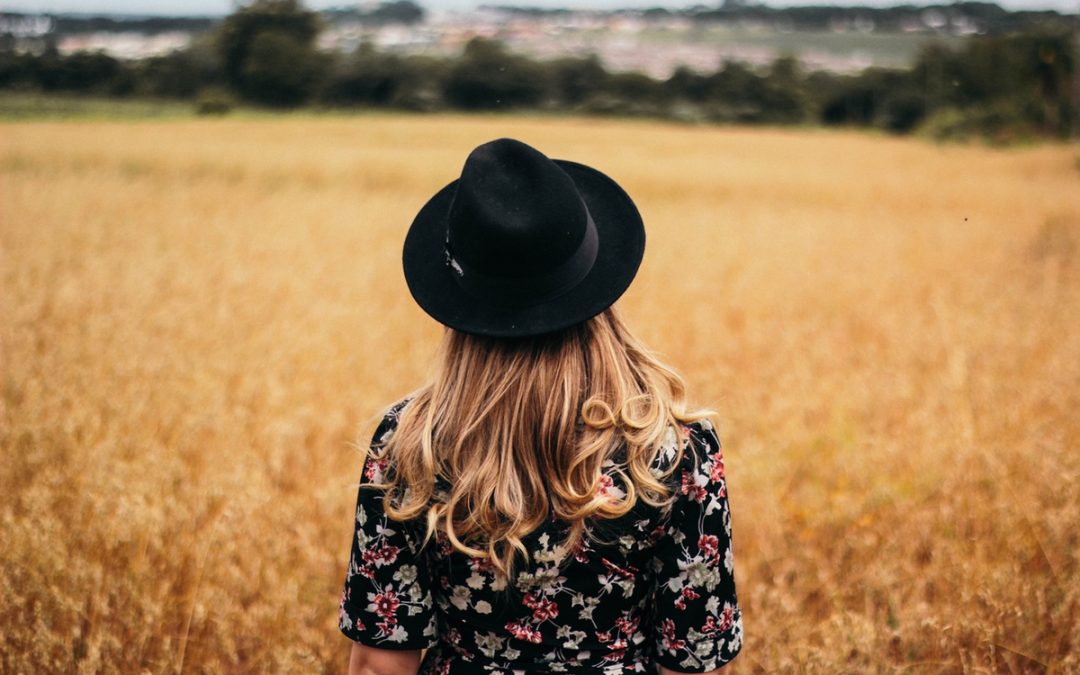 Back shot of a blonde woman with a black hat and dress