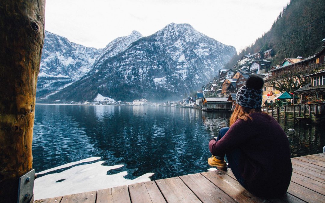 woman in purple sweater sitting on wooden floor with view of lake and mountains